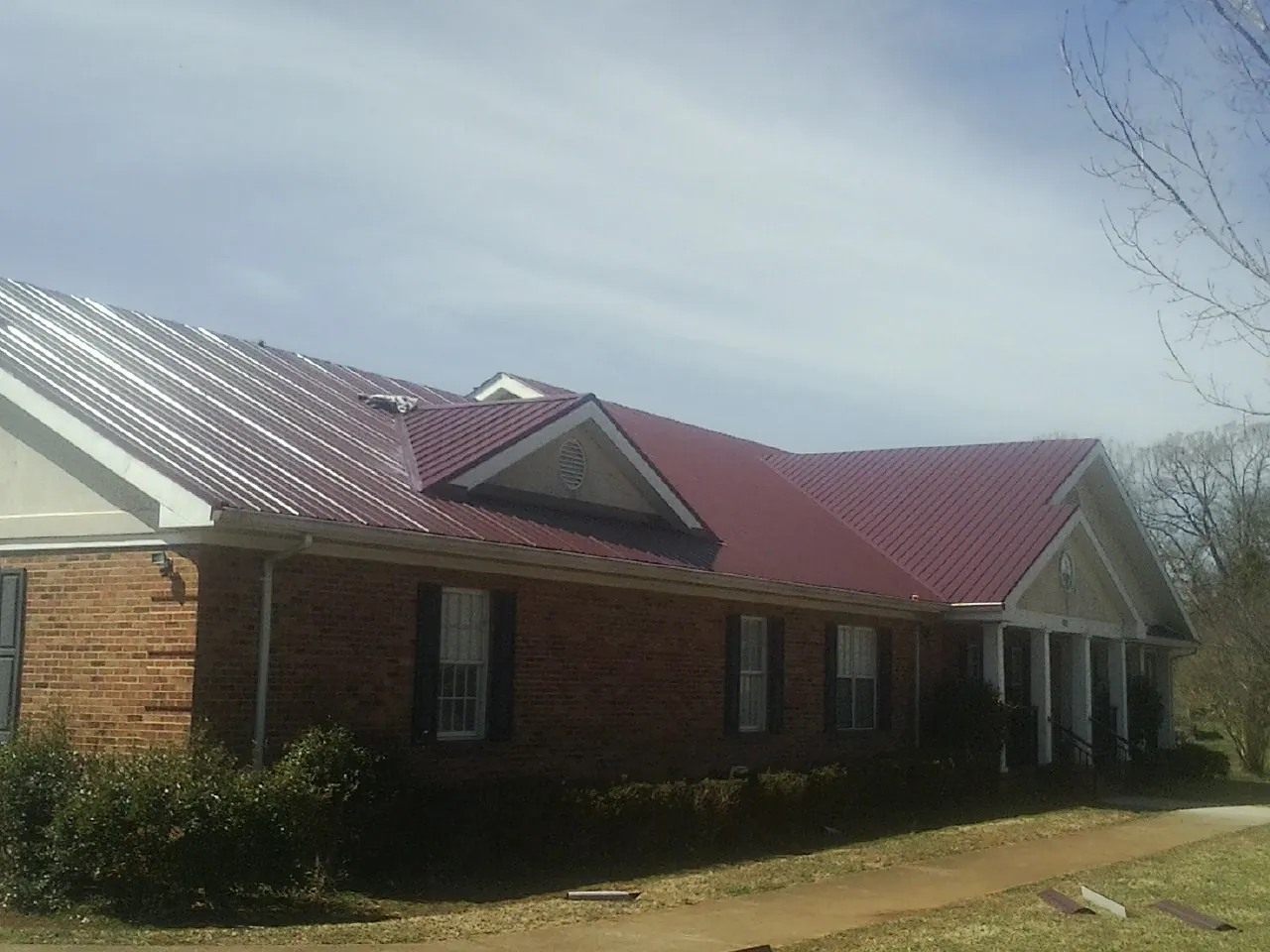 Red metal roof with gabled entries on a long brick building, from a Hail Damage Roof Repair job in Harrisburg