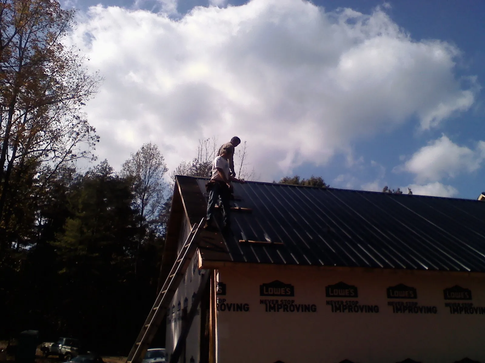 Roofer fastening dark metal panels high against a cloudy sky, from a Roof Inspection job in Harrisburg