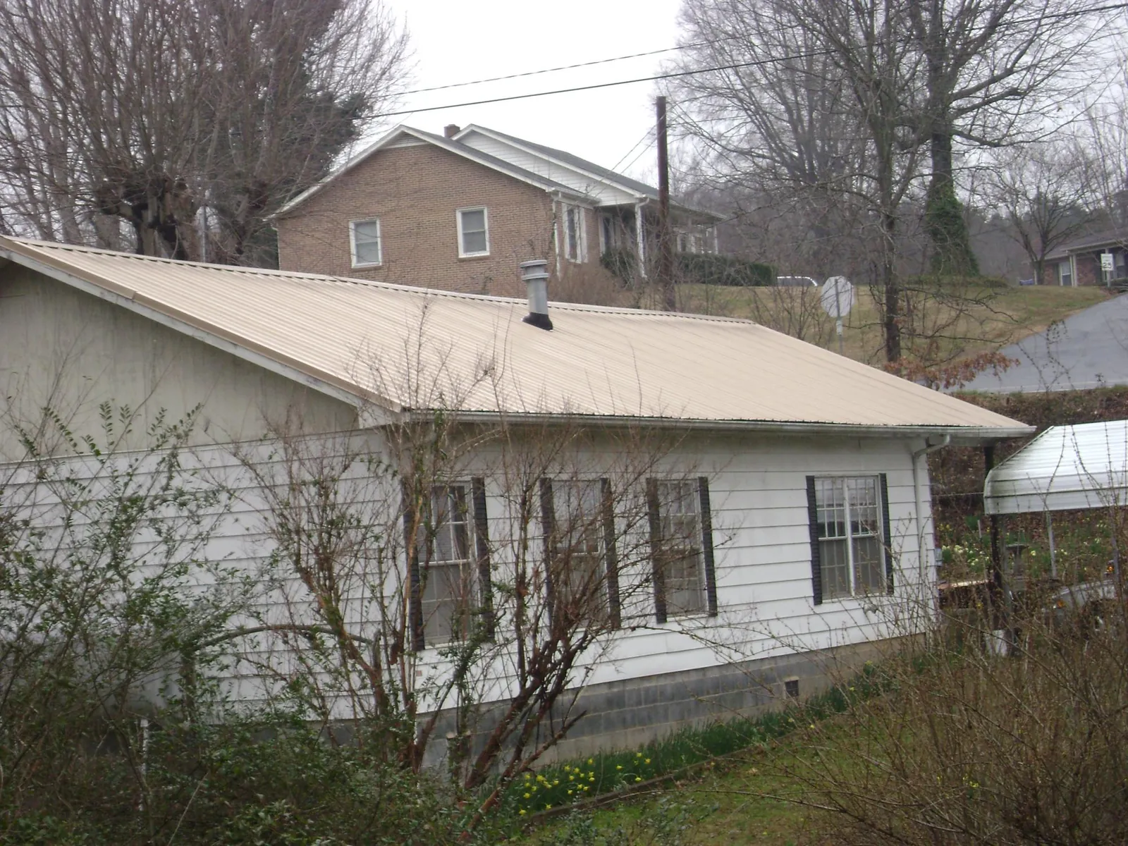 Tan metal roof on a white sided house set into a hillside — Commercial Roofing by Roofing Brothers in Harrisburg
